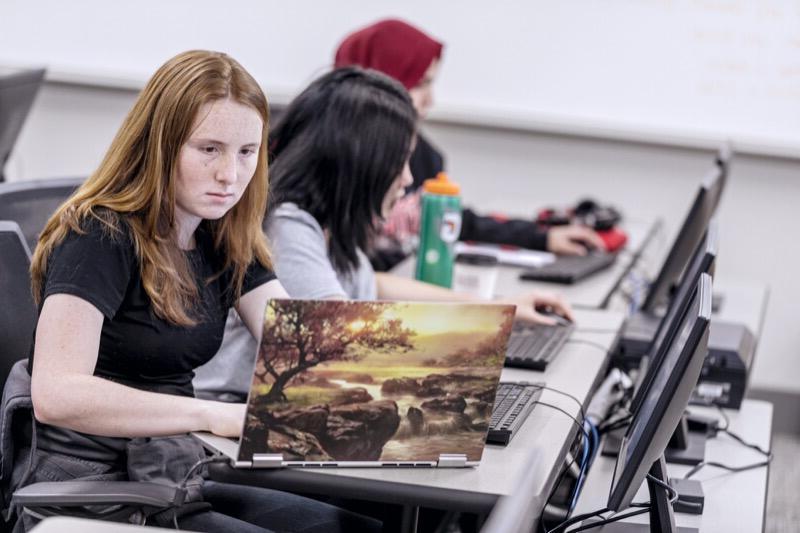 年轻的女人坐在桌子旁用笔记本电脑工作.