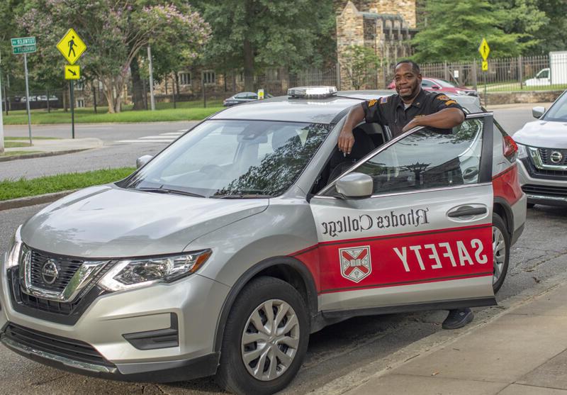 a smiling officer stands next to a campus safety car