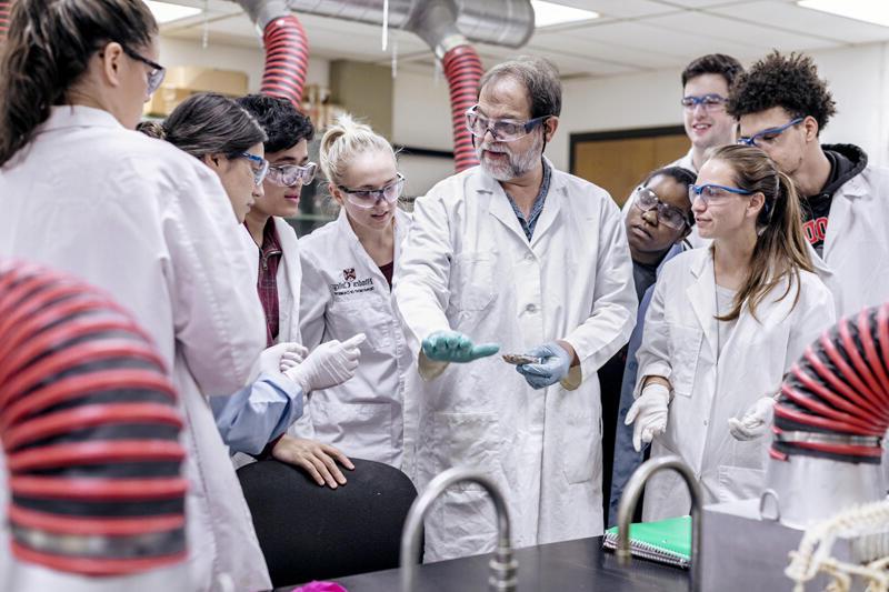 a professor shows a group of students in lab coats an experiment